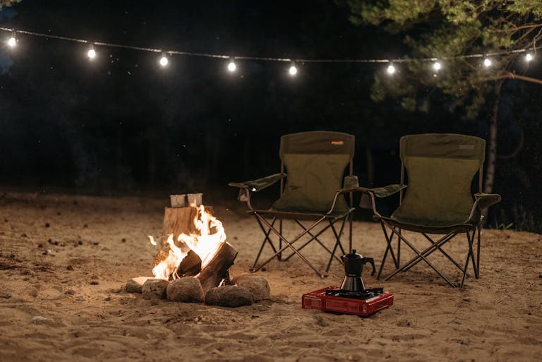 Outdoor camping scene with chairs and bonfire under string lights at night.